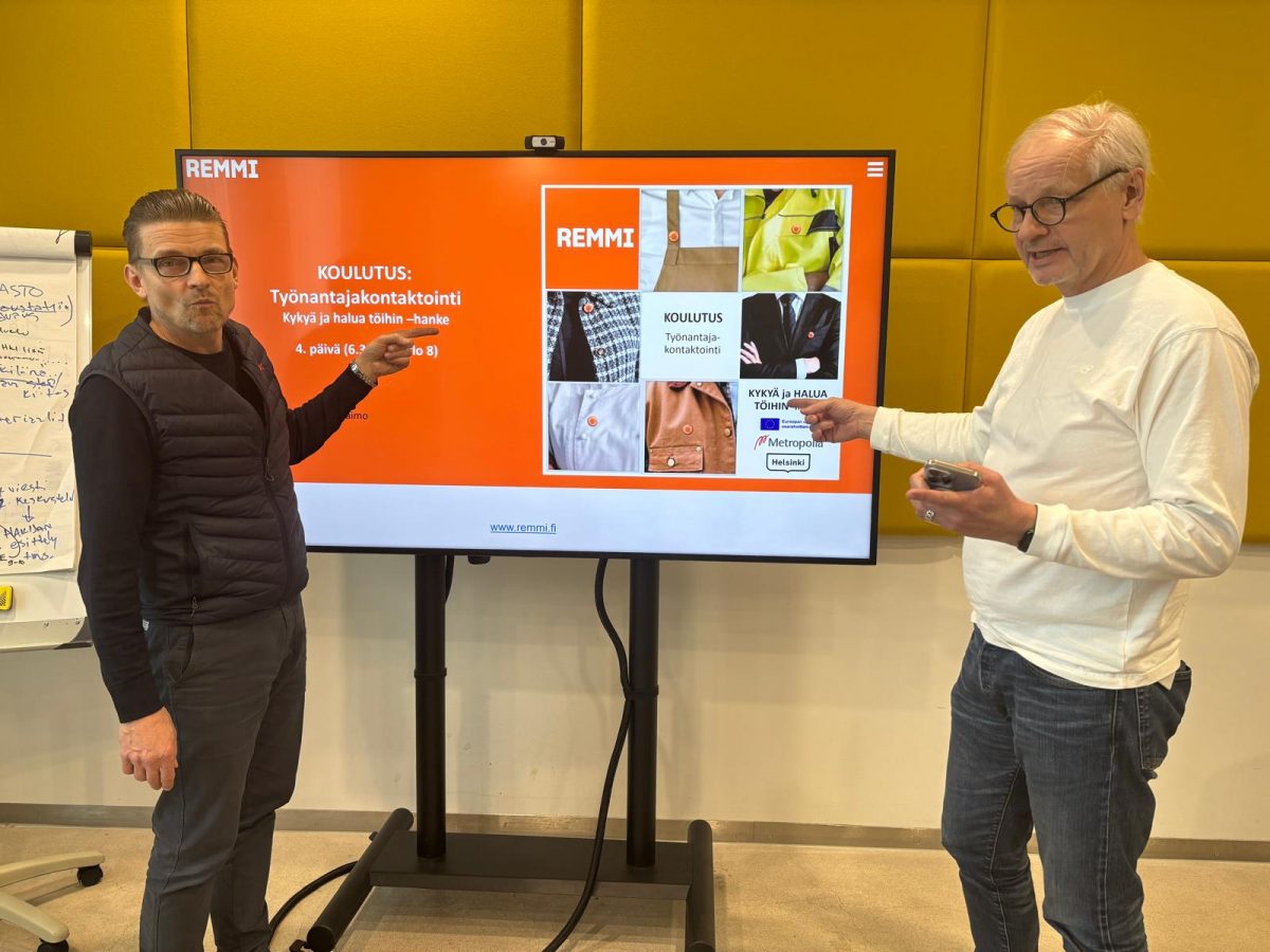 Kuvassa kaksi miestä (kouluttajat), jotka osoittavat näytölle, jossa lukee perustietoja koulutuksesta.